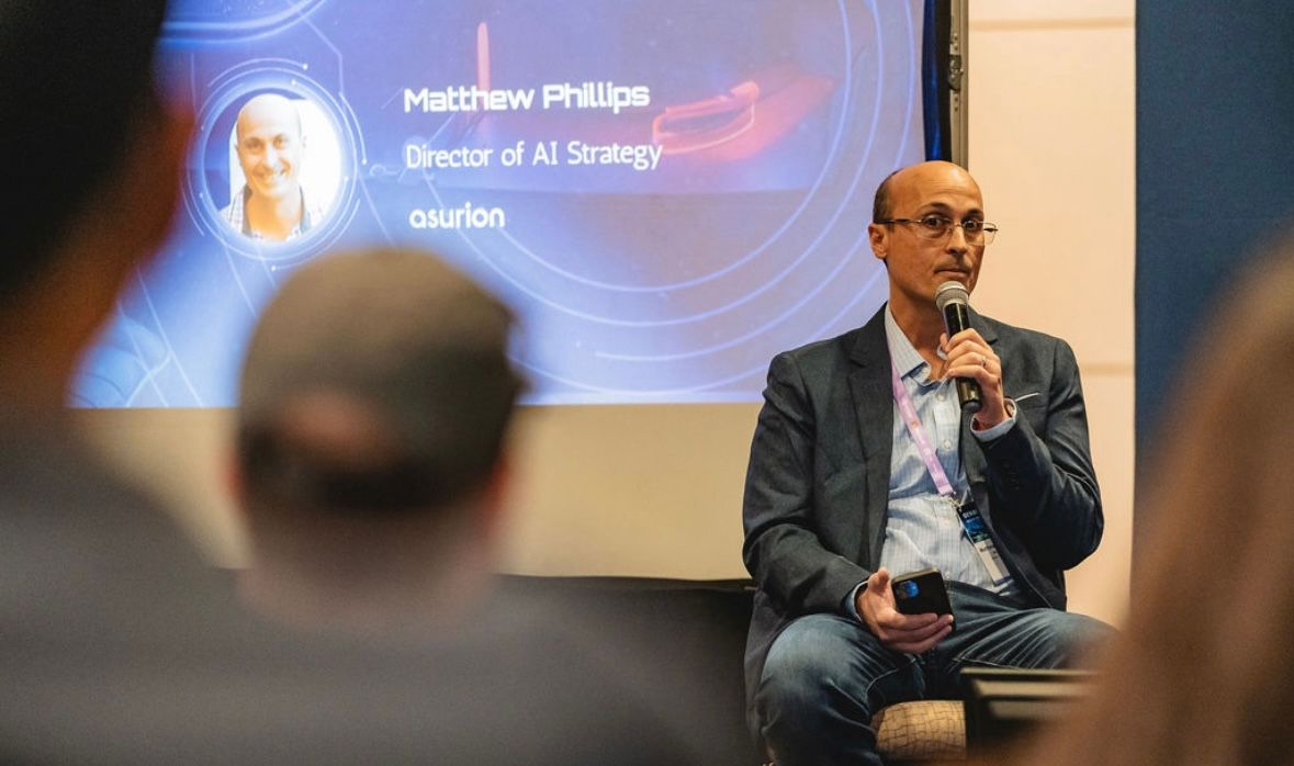 Matt Phillips seated on stage with a microphone. The screen behind him reads Matthew Phillips, Director of AI Strategy, Asurion.